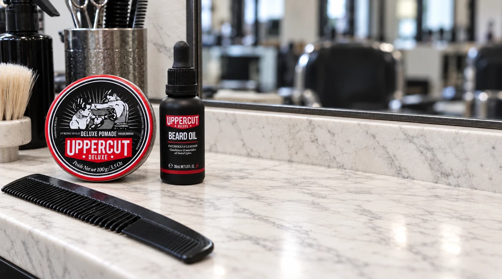 Uppercut Deluxe pomade, beard oil and a comb on the left of a marble barber station